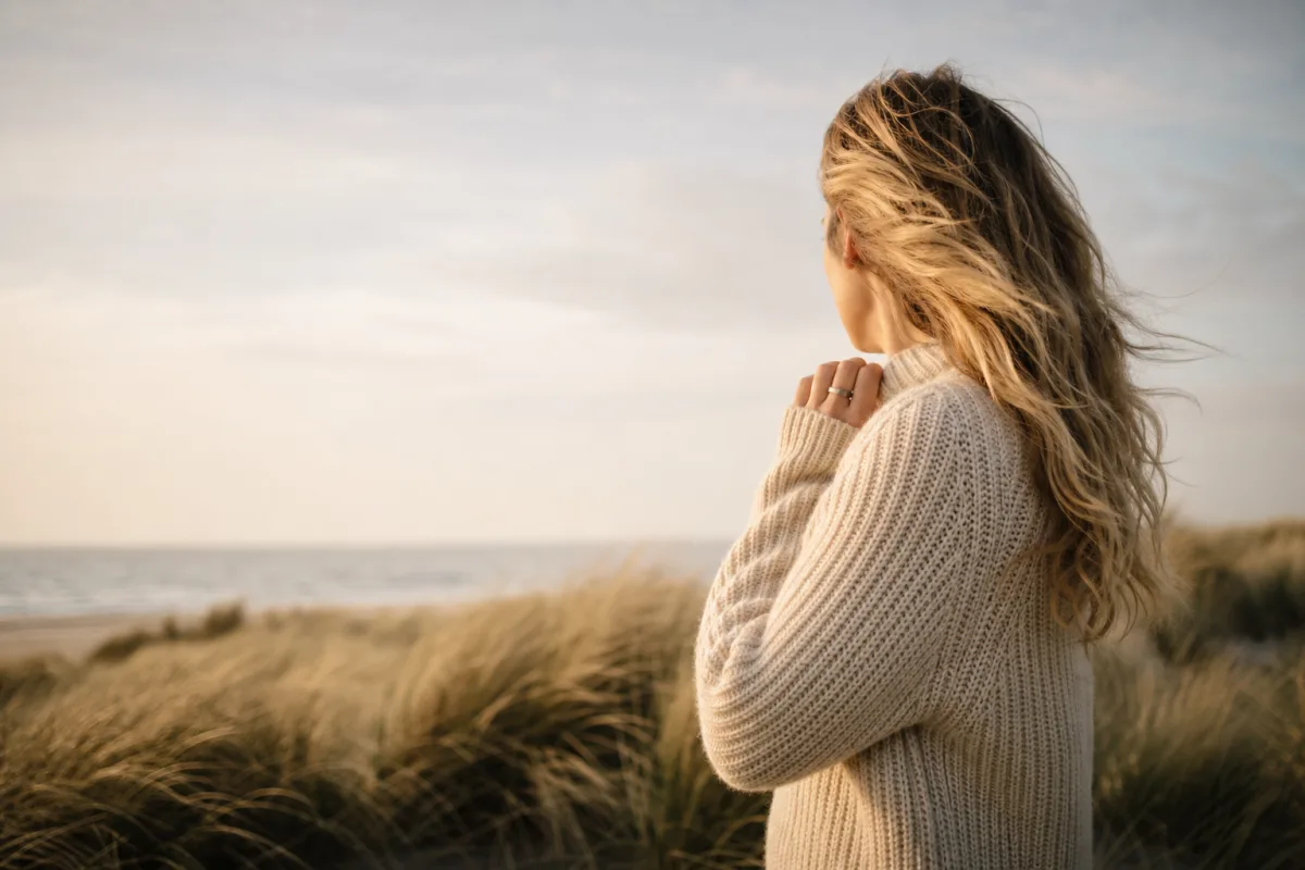 Frau im Strickpullover blickt in den Dünen aufs Meer — Ruhe an der Nordsee